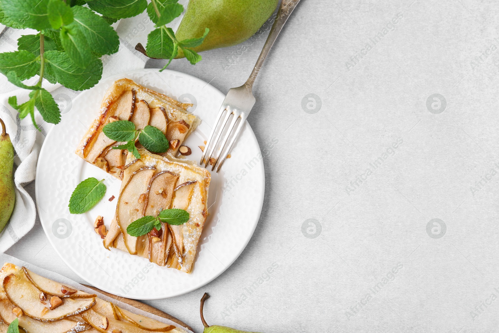 Photo of Pieces of tasty puff pastry pie with pears and mint on light grey table, top view. Space for text