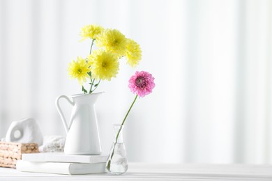 Photo of Beautiful flowers in vases and books on white wooden table at home. Space for text