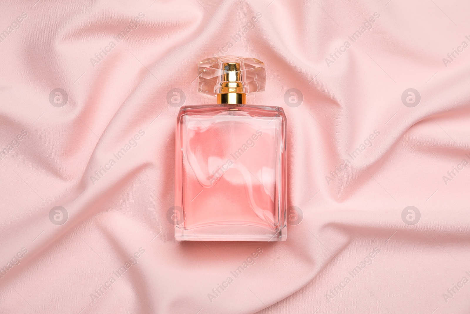 Photo of Bottle of perfume on pink silk fabric, top view