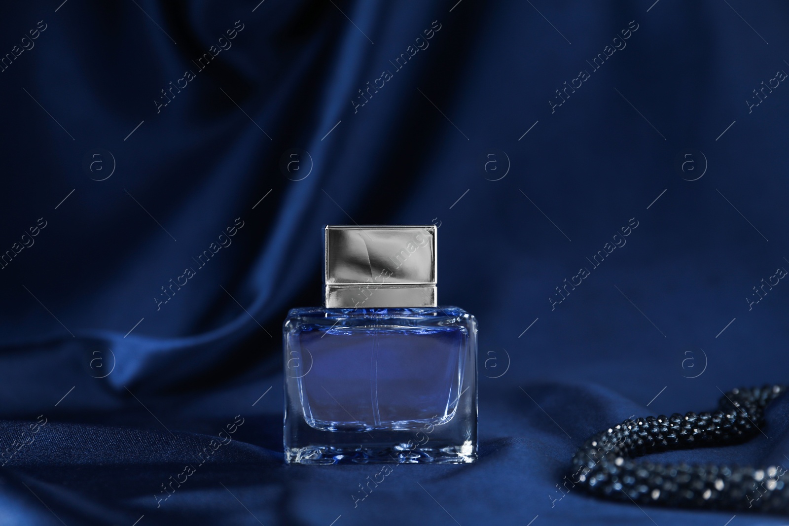 Photo of Bottle of perfume and dark blue silk fabric