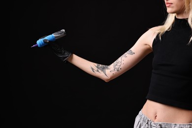 Professional artist in gloves holding tattoo machine on black background, closeup. Space for text