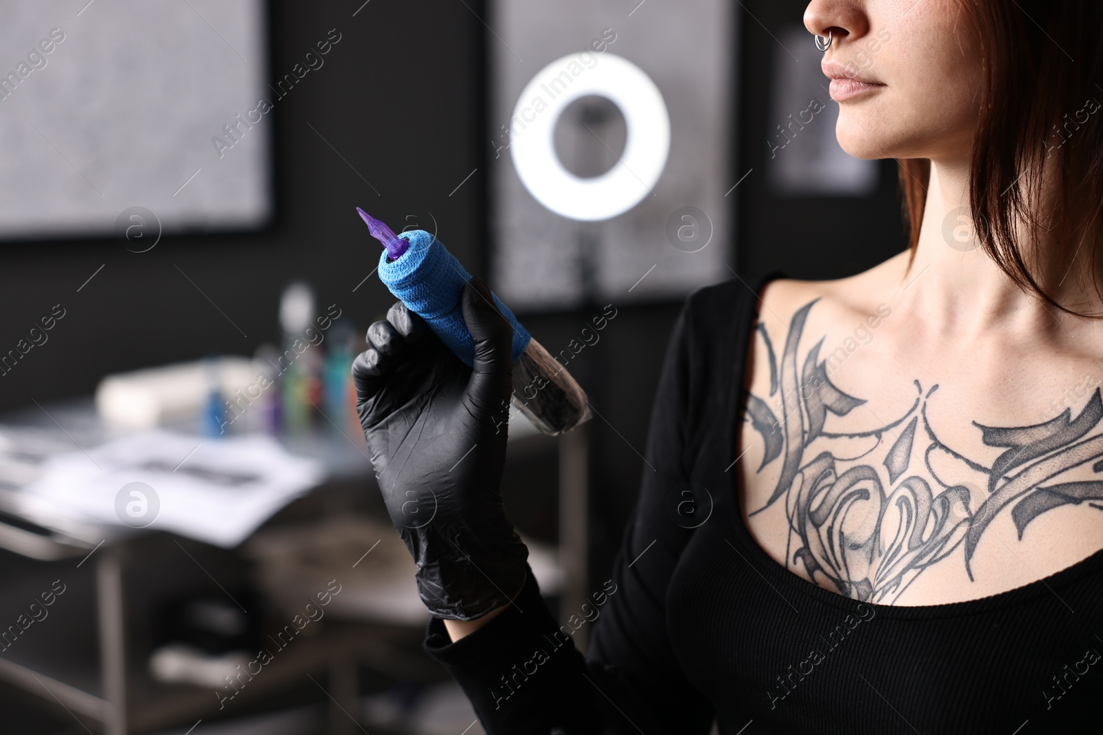 Photo of Professional artist in gloves with tattoo machine in salon, closeup. Space for text