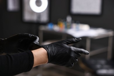 Photo of Professional tattoo artist wearing gloves in salon, closeup. Space for text