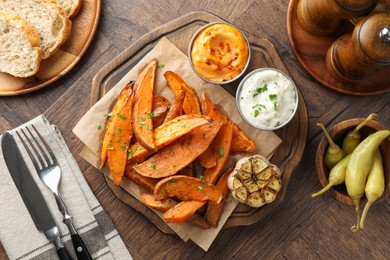 Photo of Tasty cooked sweet potatoes served with sauces on wooden table, top view