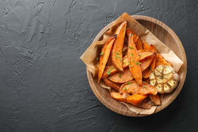 Photo of Tasty cooked sweet potatoes with parsley and garlic on black table, top view. Space for text