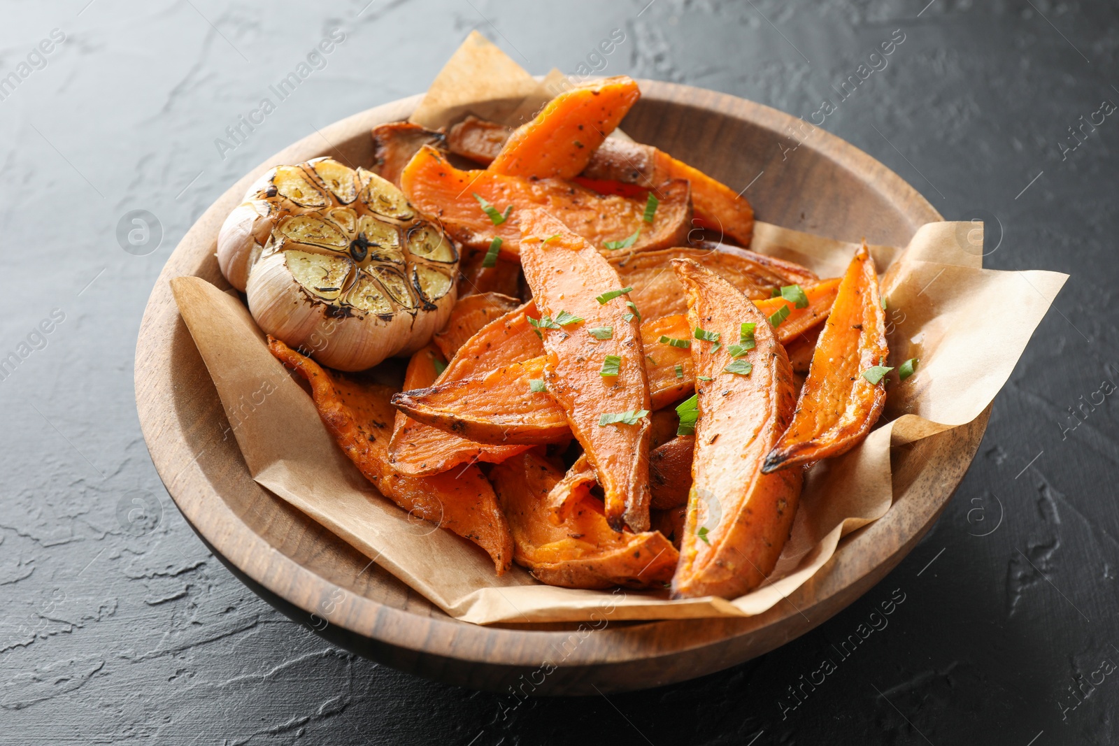 Photo of Tasty cooked sweet potatoes with parsley and garlic on black table, closeup