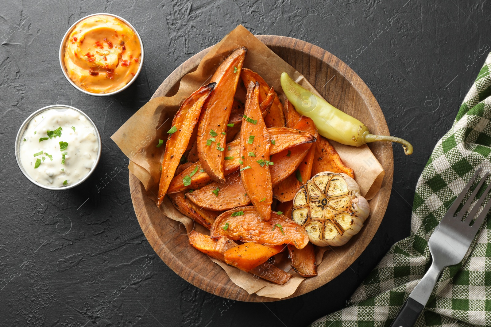 Photo of Tasty cooked sweet potatoes with garlic, pickled pepper and sauces on black table, top view