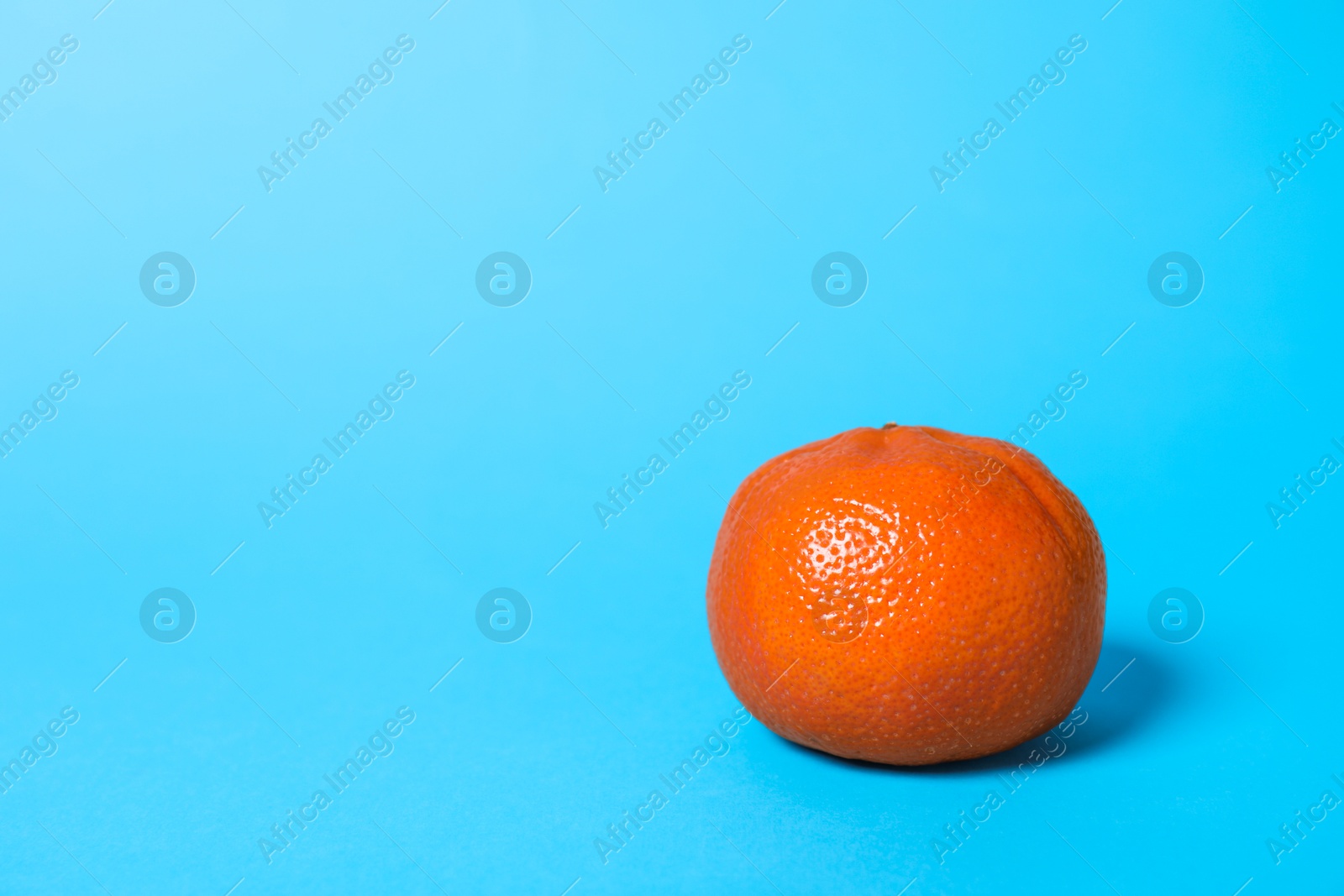 Photo of Fresh ripe tangerine on light blue background. Space for text