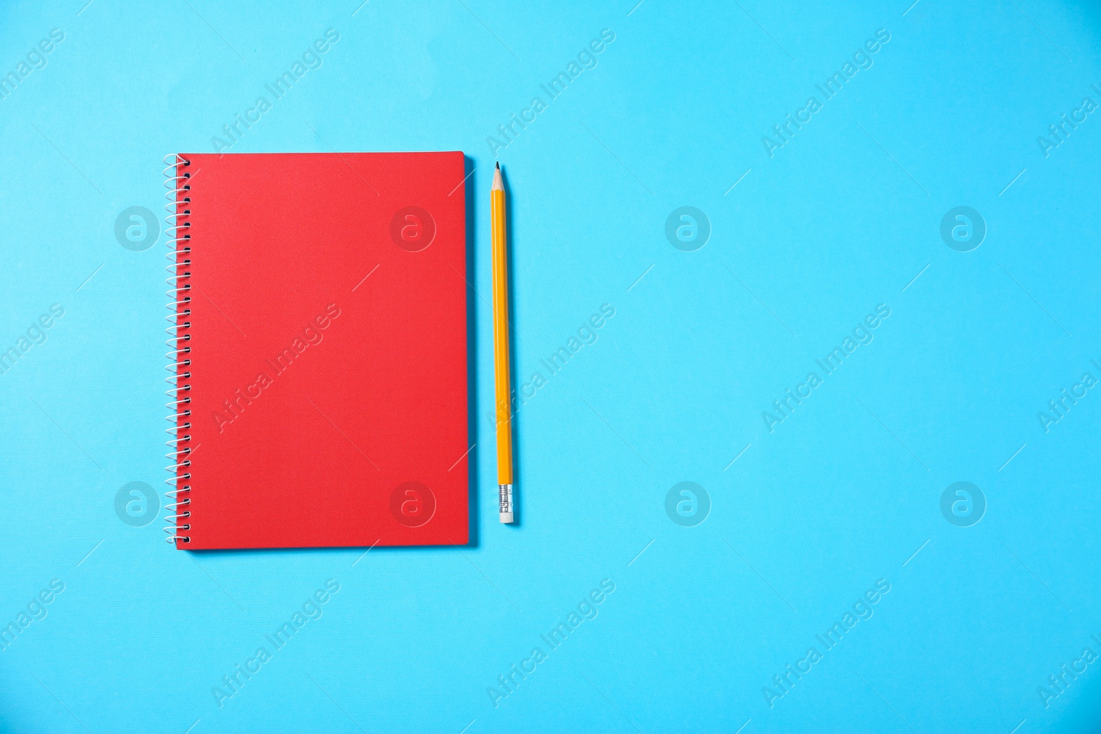 Photo of Notebook and pencil on light blue background, top view. Space for text