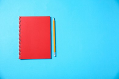 Notebook and pencil on light blue background, top view. Space for text