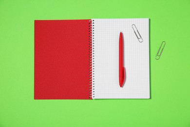 Photo of Notebook, paper clips and pen on light green background, top view