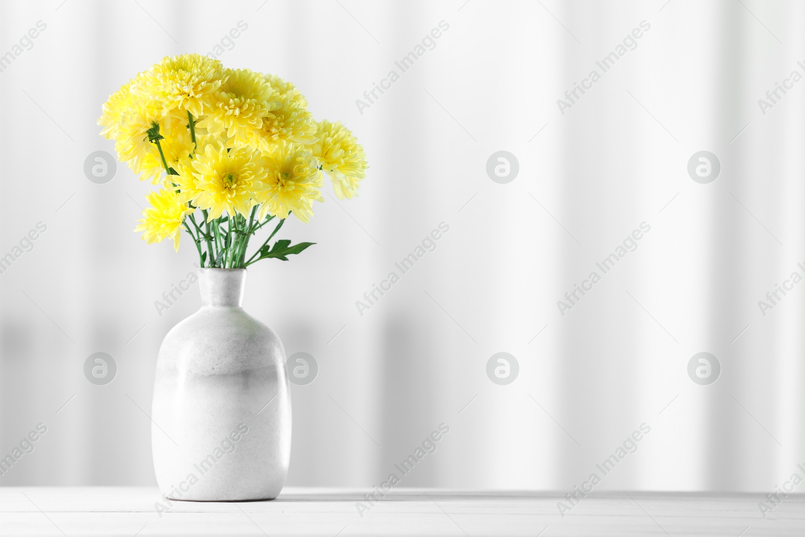 Beautiful yellow flowers in vase on white wooden table at home. Space for text Photo of Beautiful yellow flowers in vase on white wooden table at home. Space for text