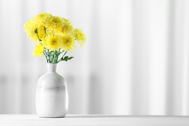 Photo of Beautiful yellow flowers in vase on white wooden table at home. Space for text