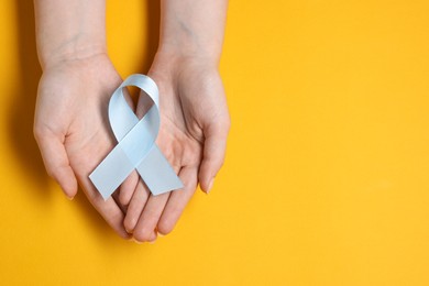 Photo of Woman with light blue ribbon on yellow background, top view and space for text. Childhood cancer awareness