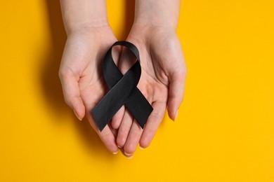 Photo of Woman with black ribbon on yellow background, top view. Melanoma and mourning concept