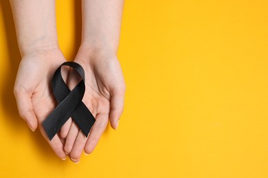 Photo of Woman with black ribbon on yellow background, top view with space for text. Melanoma and mourning concept