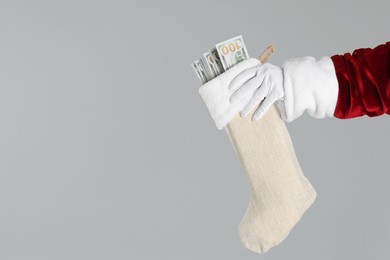 Photo of Santa Claus holding stocking with dollar banknotes on gray background, closeup. Space for text