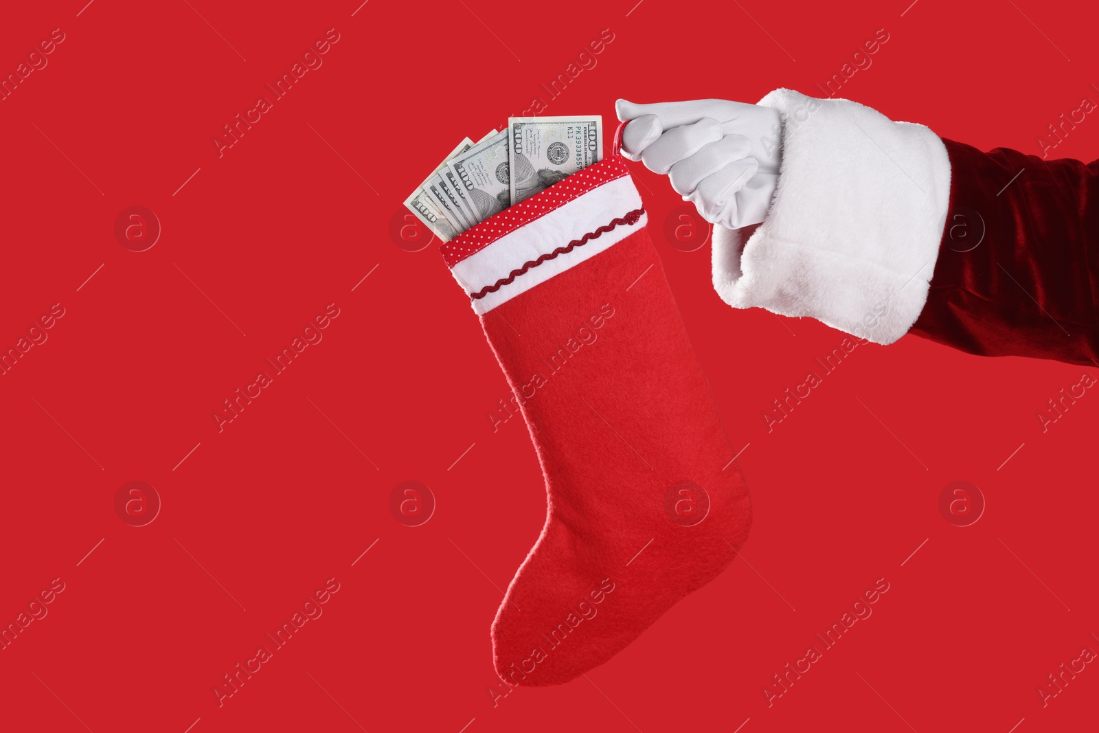 Photo of Santa Claus holding stocking with dollar banknotes on red background, closeup. Space for text