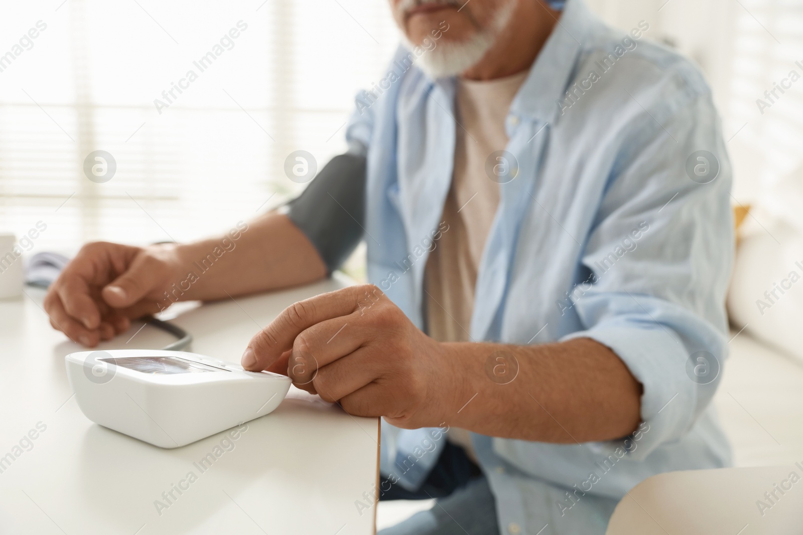 Photo of Senior man measuring blood pressure at table indoors, closeup