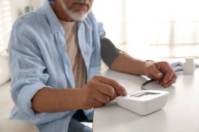 Photo of Senior man measuring blood pressure at table indoors, closeup