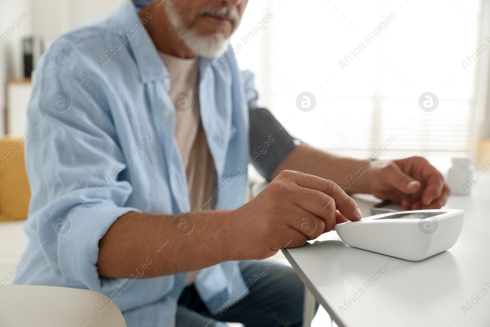 Photo of Senior man measuring blood pressure at table indoors, closeup