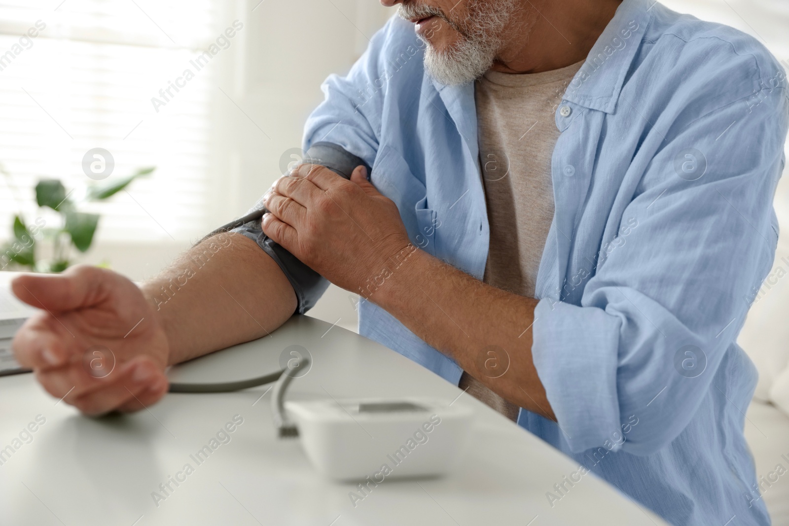 Photo of Senior man measuring blood pressure at table indoors, closeup