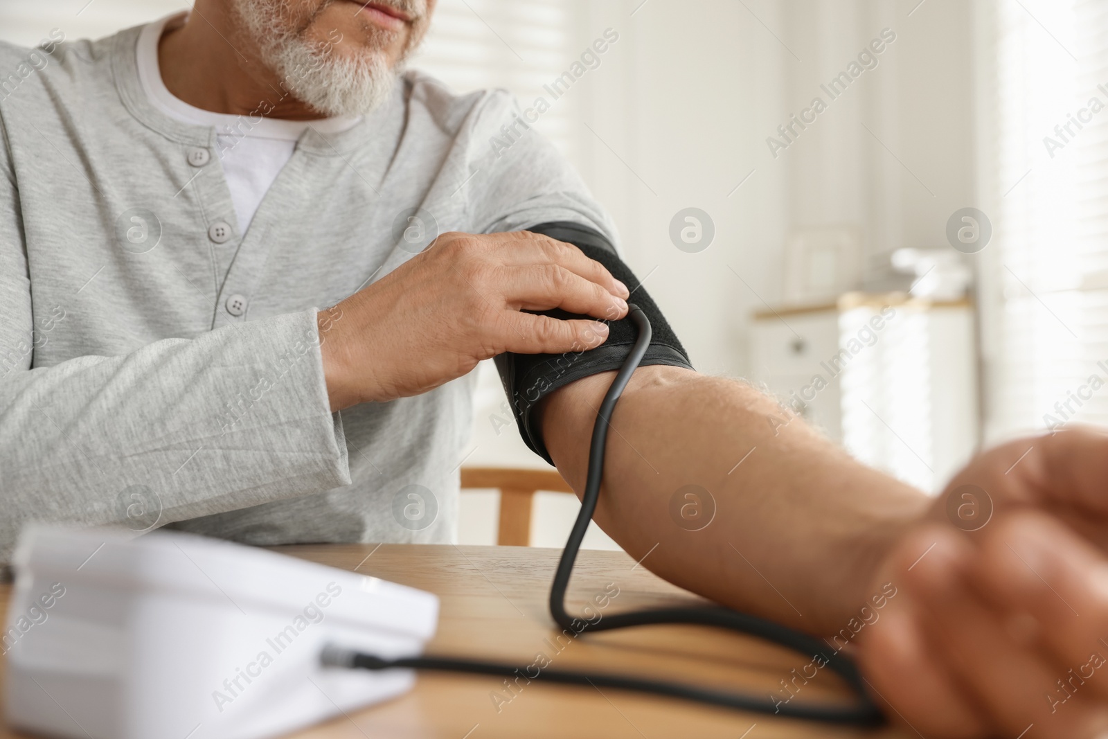 Photo of Senior man measuring blood pressure at table indoors, closeup