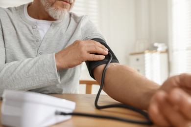 Photo of Senior man measuring blood pressure at table indoors, closeup