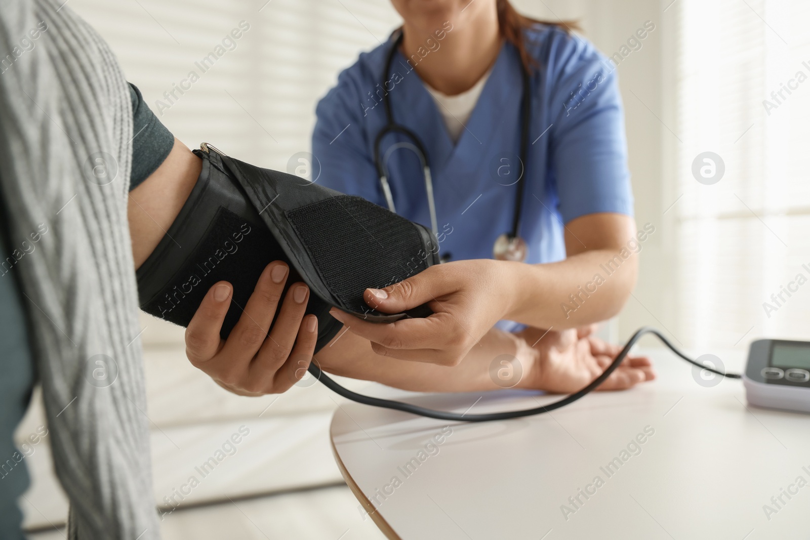 Photo of Doctor measuring patient's blood pressure at table indoors, closeup