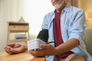 Photo of Senior man measuring blood pressure at table indoors, closeup