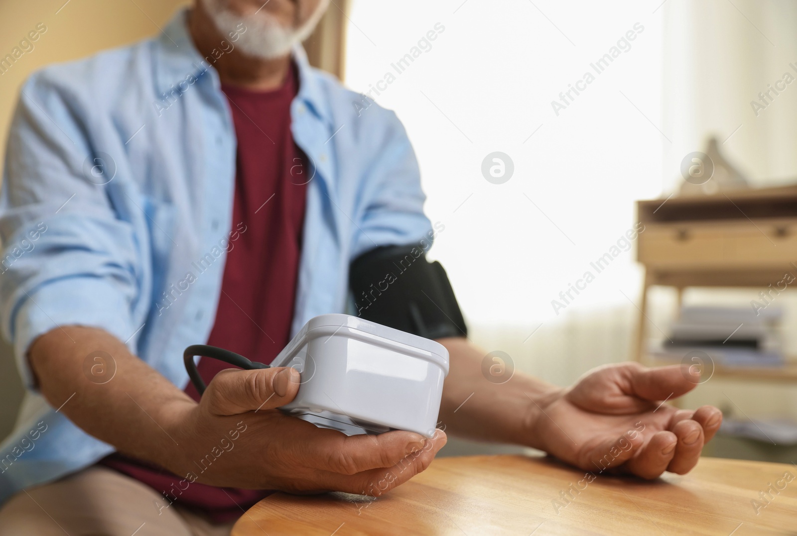 Photo of Senior man measuring blood pressure at table indoors, closeup