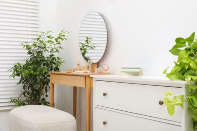 Photo of Mirror, dressing table, houseplants, pouffe and chest of drawers indoors. Interior design