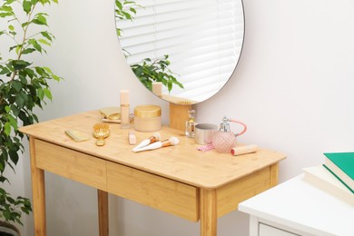 Photo of Mirror, dressing table with cosmetic products and houseplant indoors. Interior design