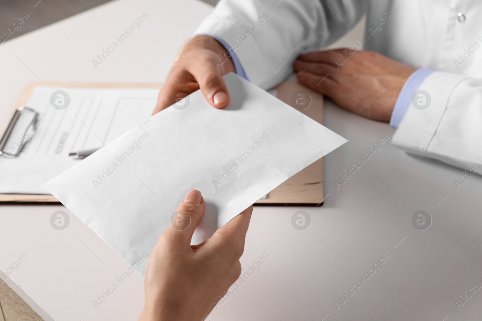 Photo of Corruption concept. Woman giving envelope with money to doctor at white table, closeup