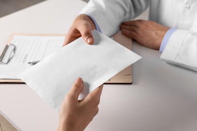 Photo of Corruption concept. Woman giving envelope with money to doctor at white table, closeup