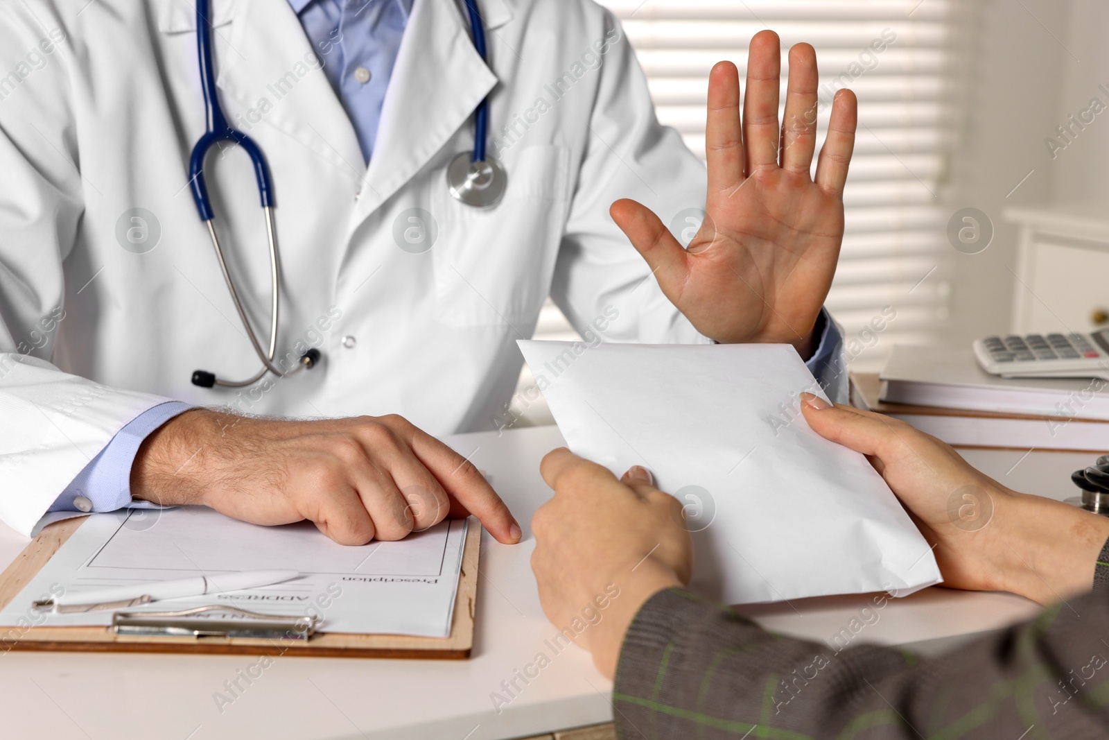 Photo of Corruption concept. Woman giving envelope with money to doctor at white table, closeup