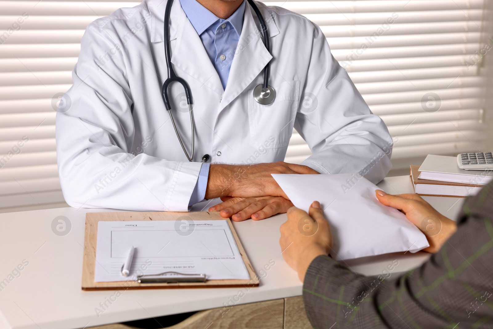 Photo of Corruption concept. Woman giving envelope with money to doctor at white table, closeup