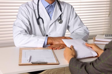 Photo of Corruption concept. Woman giving envelope with money to doctor at white table, closeup