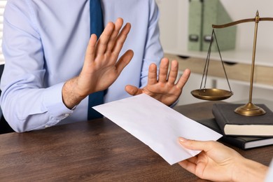 Photo of Corruption concept. Woman giving envelope with money to man at wooden table, closeup