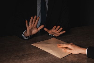 Photo of Corruption concept. Woman giving envelope with money to man at wooden table, closeup