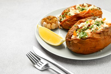 Photo of Tasty baked sweet potatoes with feta cheese, parsley and lemon slice on light textured table, closeup. Space for text