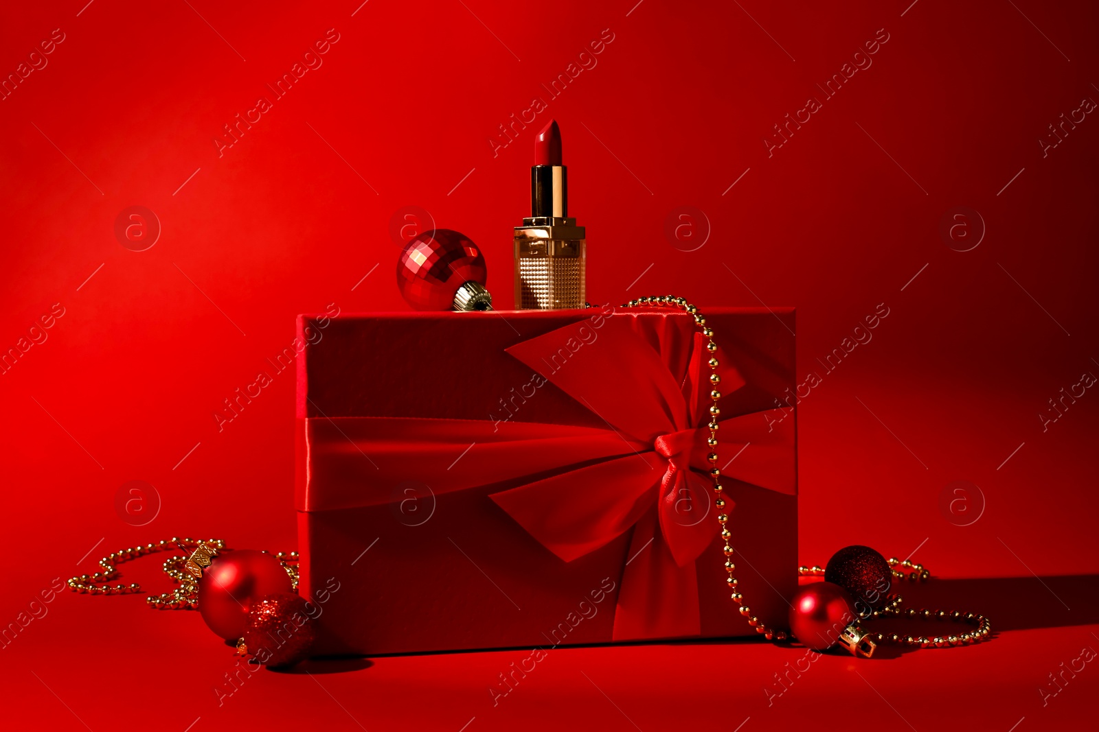 Photo of Christmas present. Lipstick, gift box and festive decor on red background