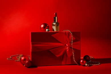 Photo of Christmas present. Lipstick, gift box and festive decor on red background