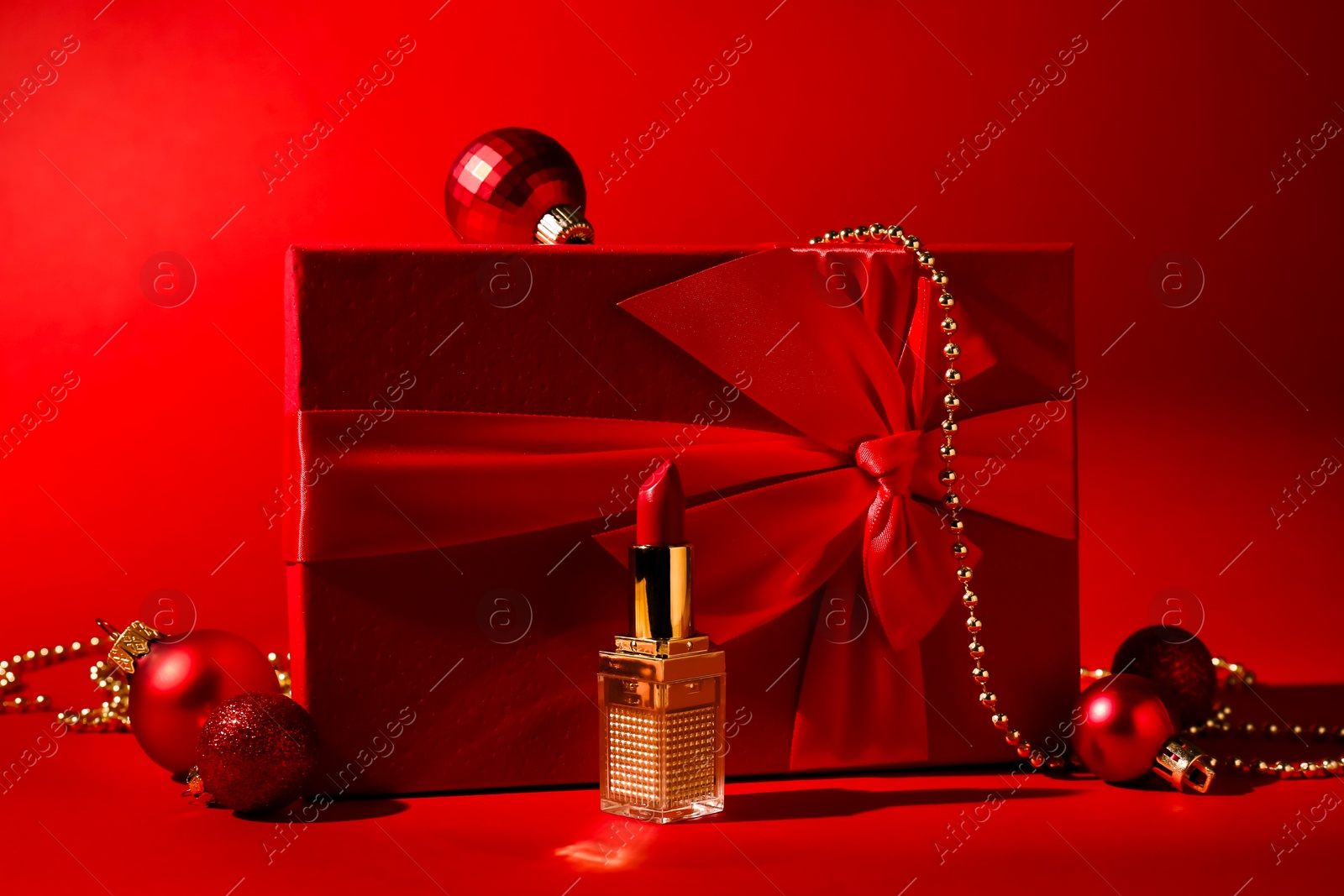 Photo of Christmas present. Lipstick, gift box and festive decor on red background