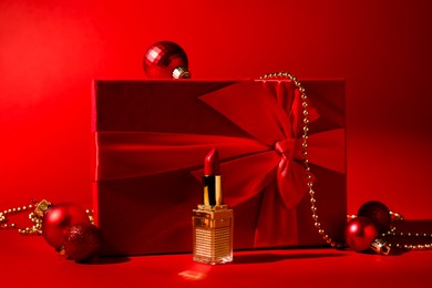 Photo of Christmas present. Lipstick, gift box and festive decor on red background