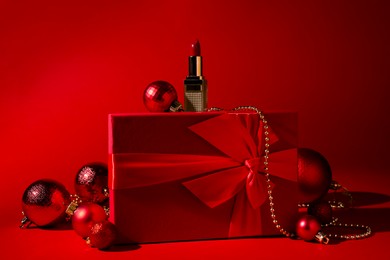 Photo of Christmas present. Lipstick, gift box and festive decor on red background