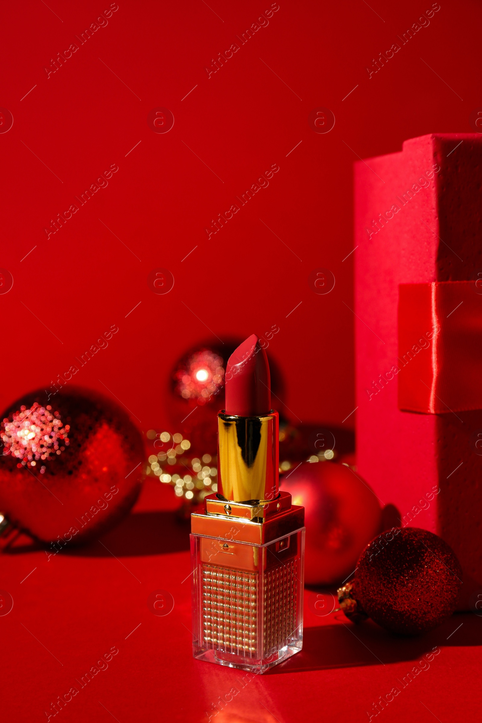 Photo of Christmas gift. Lipstick and festive decor on red background