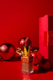 Photo of Christmas gift. Lipstick and festive decor on red background