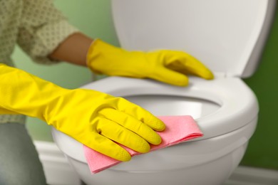 Photo of Woman cleaning toilet seat in restroom, closeup