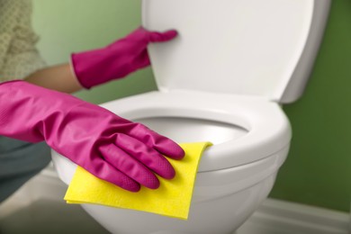 Photo of Woman cleaning toilet seat in restroom, closeup